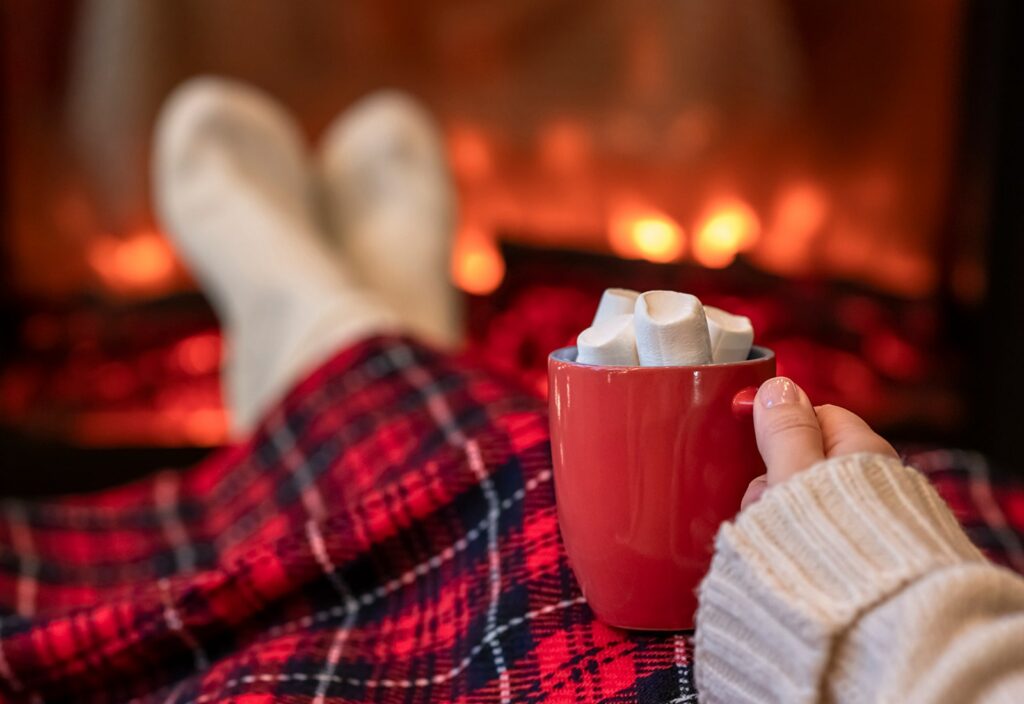 Selecting Seasonal Throw Blankets Feature - plaid throw blanket on the lap of a woman enjoying hot chocolatye