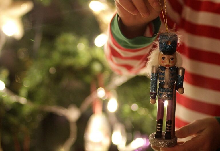 nutcracker ornaments tradition feature - child holding a nutcracker ornament in front of a lit Christmas tree